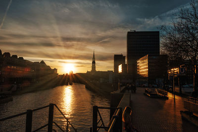 Buildings by river against sky during sunset