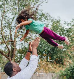 Black or african american father in white shirt in the back yard playing with mixed race daughter