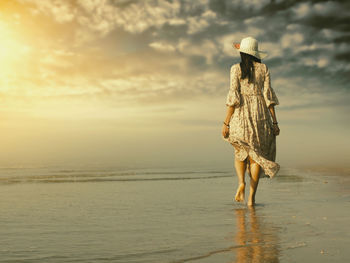 Woman with umbrella on beach against sky during sunset