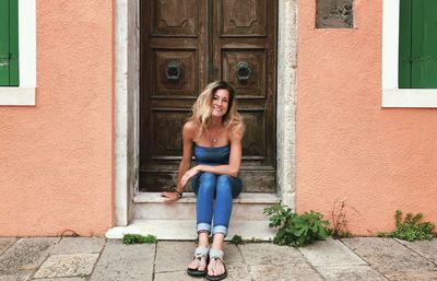 Full length portrait of smiling woman sitting at door