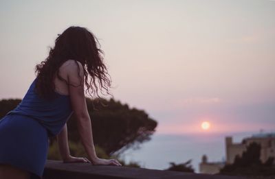 Side view of woman with arms raised against sky during sunset