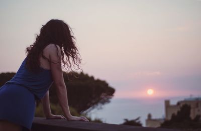 Side view of woman by retaining wall against sky during sunset