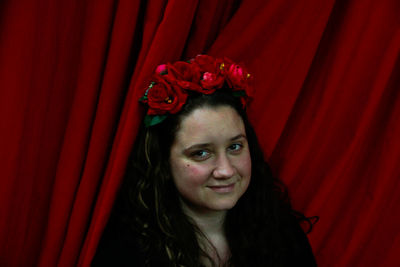 Portrait of beautiful young woman with red flower against curtain