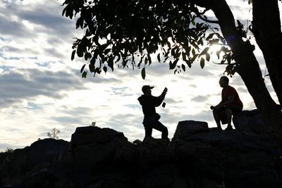 Low angle view of silhouette woman standing on rock against sky