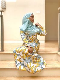 Full length of young woman wearing hijab while sitting on staircase at home