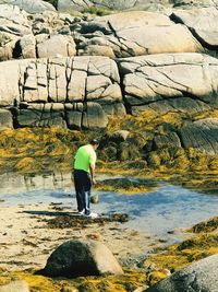 Rear view of man standing by rocks at beach 