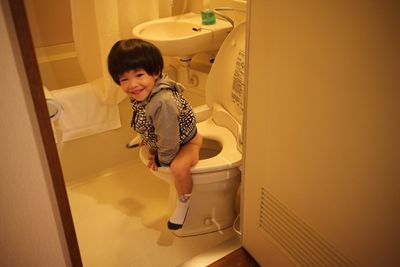 Cute boy sitting on toilet bowl at bathroom