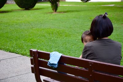 Rear view of mother and daughter sitting on bench in park
