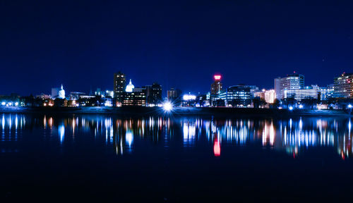 Reflection of illuminated buildings in river against sky at night