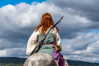 Rear view of woman sitting on horse against cloudy sky