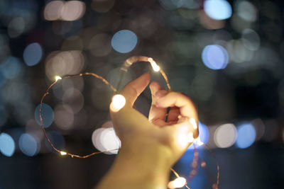 Cropped hand of woman holding illuminated string lights