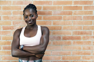 Portrait of smiling young woman against brick wall