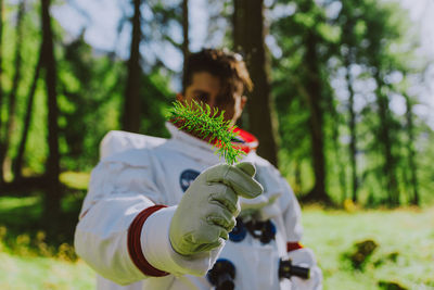 Portrait of man holding plant against trees