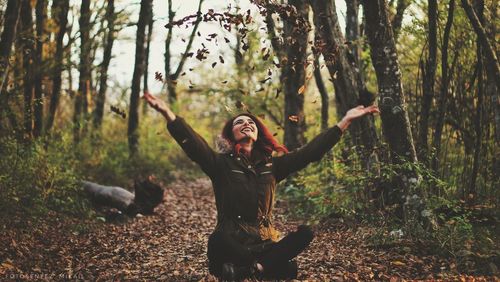 Woman throwing autumn leaves while sitting in forest