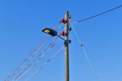 Low angle view of telephone pole against clear blue sky