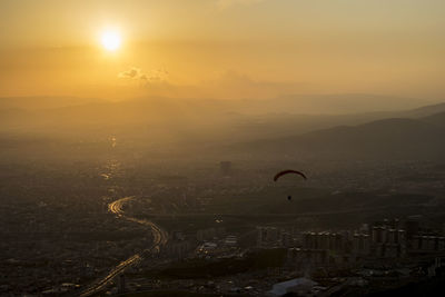 Person paragliding over city against sky during sunrise