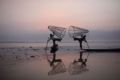 Fishermen fishing in lake against sky during sunset