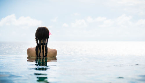 Rear view of woman in infinity pool against sea