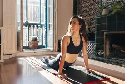 Active young woman looking away while practicing cobra pose at home