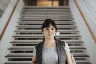 Portrait of confident female professor standing against steps in university