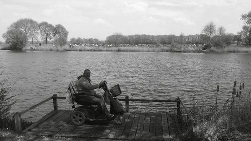 Man sitting on lake against sky