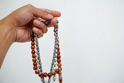 Cropped hand holding prayer beads over gray background