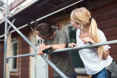 Couple leaning on scaffolding outside house during home improvement