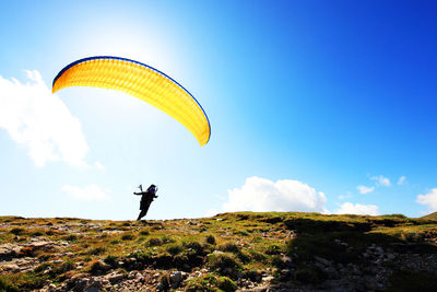 Man with parachute on field against sky