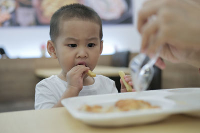 Cropped hands of mother feeding son on table in restaurant