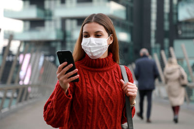 Woman wearing mask using smart phone standing outdoors