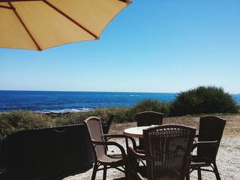 Chairs and table on beach against clear blue sky