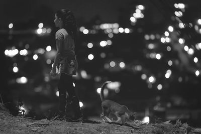 Rear view of woman with dog against illuminated lights at night