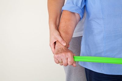 Midsection of woman assisting female in stretching belt against white background