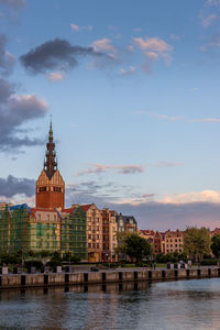 Buildings at waterfront against cloudy sky