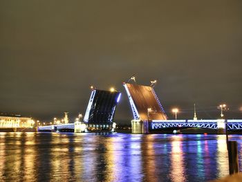 Illuminated city by sea against sky at night