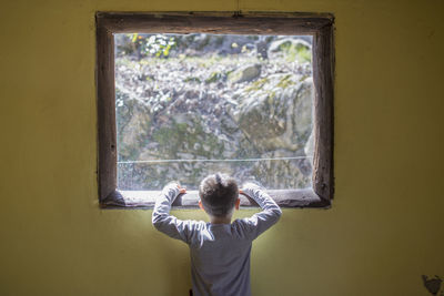 Rear view of boy looking through window at home