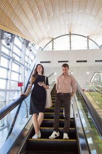 Full length of smiling young woman with man standing on escalator