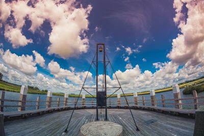 Metal structure on pier against cloudy sky