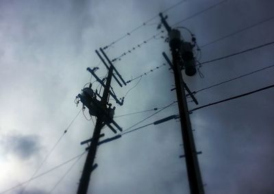 Low angle view of electricity pylon against cloudy sky