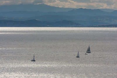 Sailboats sailing on sea against mountains