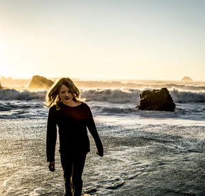 Boy walking against waves in sea at beach during sunset