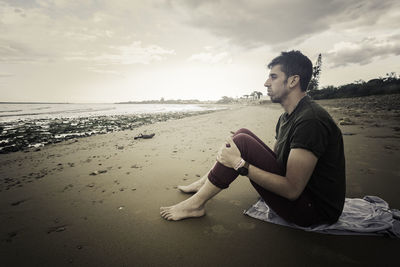 Side view of young man sitting on sand at beach