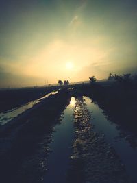 Scenic view of road by canal against sky during sunset