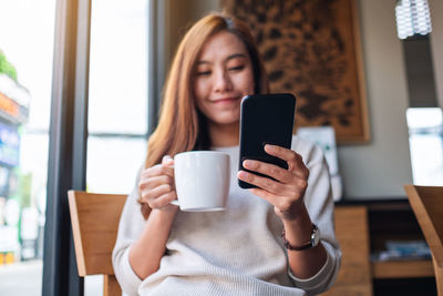 A beautiful asian woman holding and using mobile phone while drinking coffee in cafe