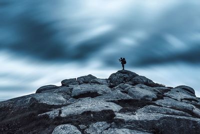 Mid distance of hiker standing on rocky mountain against sky