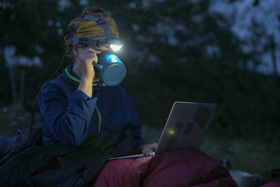 Woman using laptop while camping on field at dusk