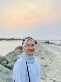 Portrait of smiling young woman standing at beach during sunset