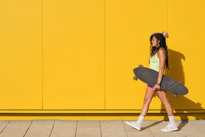 Woman with umbrella against yellow wall