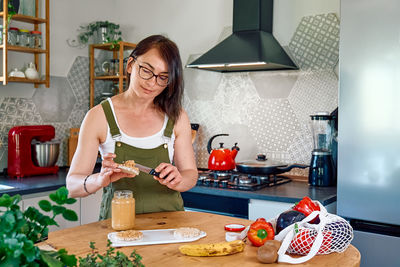 Woman making healthy breakfast or brunch, spreading peanut butter on a puffed corn cakes