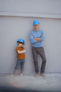 Confident senior man and grandson with arms crossed in front of wall